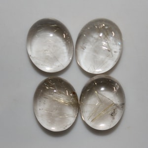 May include: Four oval-shaped, clear quartz cabochons with gold rutilated inclusions. The cabochons are smooth and polished.