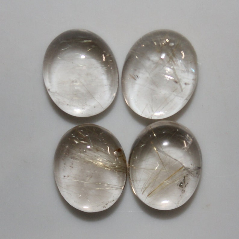 May include: Four oval-shaped, clear quartz cabochons with gold rutilated inclusions. The cabochons are smooth and polished.