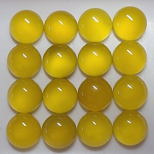 May include: Sixteen yellow, round glass cabochons arranged in a grid pattern. The cabochons have a glossy finish and vary slightly in shade, with some appearing a deeper amber color. The overall effect is a collection of vibrant, polished spheres.