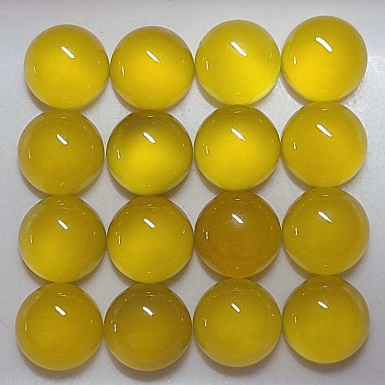 May include: Sixteen yellow, round glass cabochons arranged in a grid pattern. The cabochons have a glossy finish and vary slightly in shade, with some appearing a deeper amber color. The overall effect is a collection of vibrant, polished spheres.