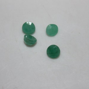 May include: Four round, green gemstones, likely emeralds, on a white surface.
