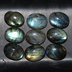 May include: Nine oval-shaped labradorite gemstones with iridescent blue, green, and gold hues. The stones are arranged in three rows of three.