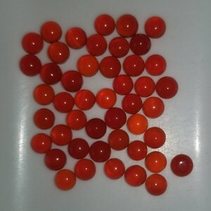 Puede incluir: Una colecci&oacute;n de aproximadamente 30 piedras preciosas redondas en cabuj&oacute;n de color rojo y naranja. Las piedras preciosas son lisas y pulidas.