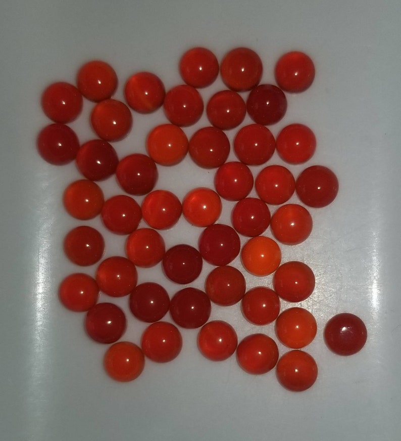 Puede incluir: Una colecci&oacute;n de aproximadamente 30 piedras preciosas redondas en cabuj&oacute;n de color rojo y naranja. Las piedras preciosas son lisas y pulidas.