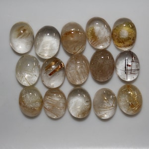 May include: A collection of 15 oval-shaped, clear quartz gemstones with gold and brown inclusions. The gemstones are arranged in three rows of five.