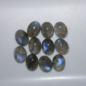May include: Ten oval-shaped labradorite gemstones with a blue iridescent sheen. The stones are arranged in a cluster on a white surface.