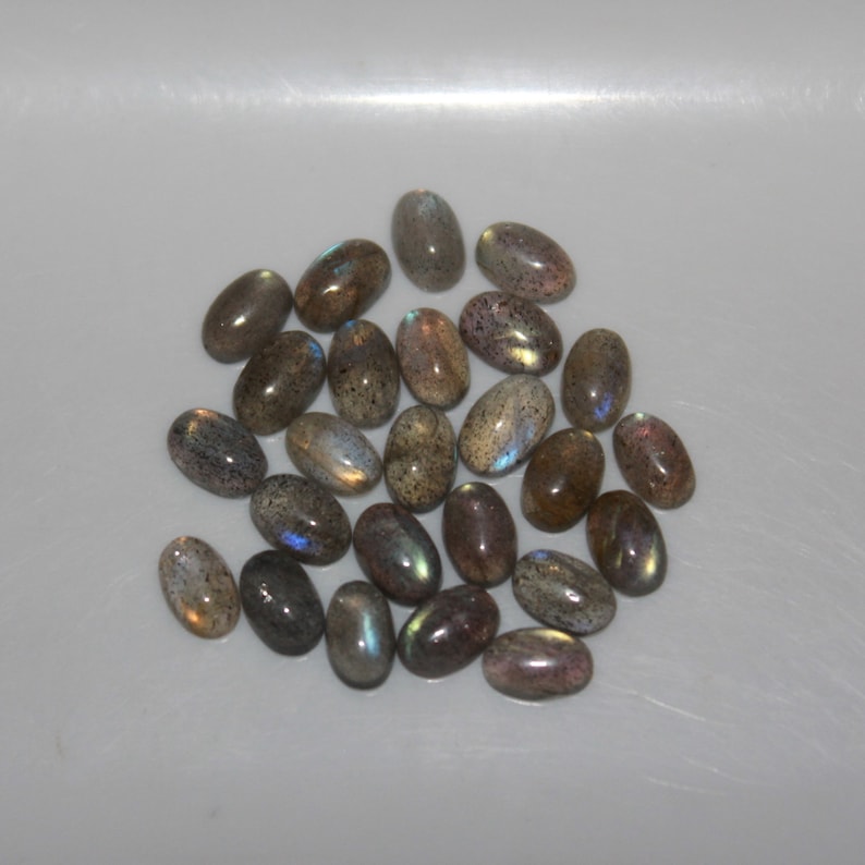 May include: A collection of oval-shaped labradorite gemstones in shades of gray with iridescent blue and green flashes.