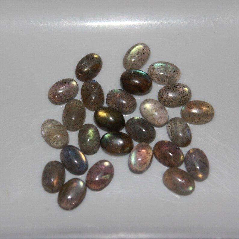 May include: A collection of oval-shaped labradorite gemstones in various shades of gray, green, and brown with iridescent flashes.
