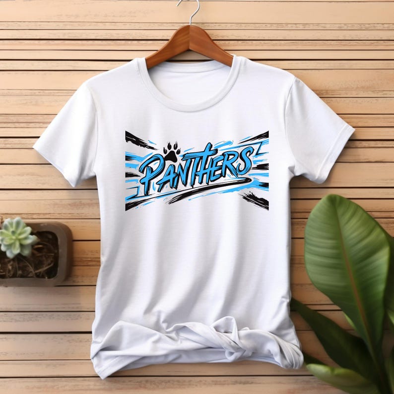 Puede incluir: Camiseta blanca con un dise&ntilde;o gr&aacute;fico azul y negro que dice "Panthers" con una huella de pata.