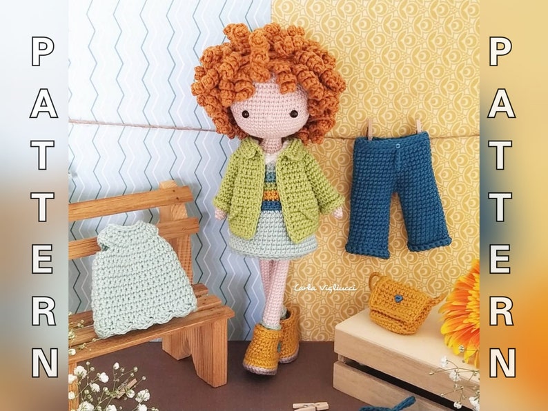 May include: Crocheted doll with curly orange hair wearing a green and yellow jacket and a light blue skirt. The doll is holding a small yellow purse. The doll is sitting on a wooden bench with a light green crocheted dress on the bench. There is a pair of blue crocheted pants hanging on a clothesline. The background is a light blue and yellow patterned wall.