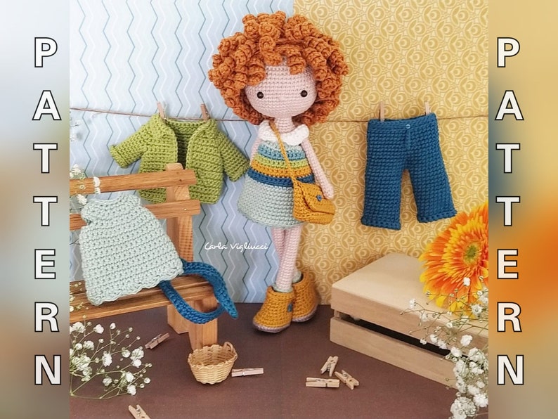 May include: Crochet doll with red hair wearing a blue and yellow dress and a brown bag. The doll is standing on a wooden bench with a green jacket, a blue dress, and a pair of blue pants hanging on it. The doll is surrounded by flowers and a wooden box.