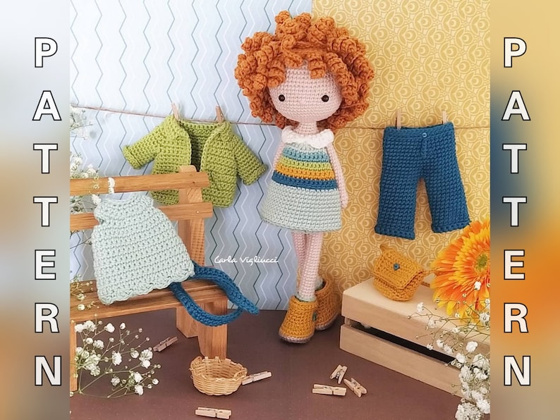 May include: A crocheted doll with red curly hair wearing a striped dress and brown boots. The doll is surrounded by crocheted clothing items, including a green cardigan, a blue pair of pants, and a light blue dress. The doll is sitting on a wooden bench with a basket and clothespins.