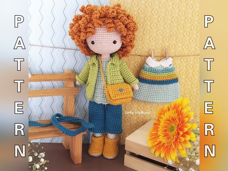 May include: Crocheted doll with curly red hair wearing a green jacket, blue jeans, and a yellow bag. The doll is holding a small crocheted bag. The doll is sitting on a wooden bench with a crocheted dress hanging on a clothesline behind it.