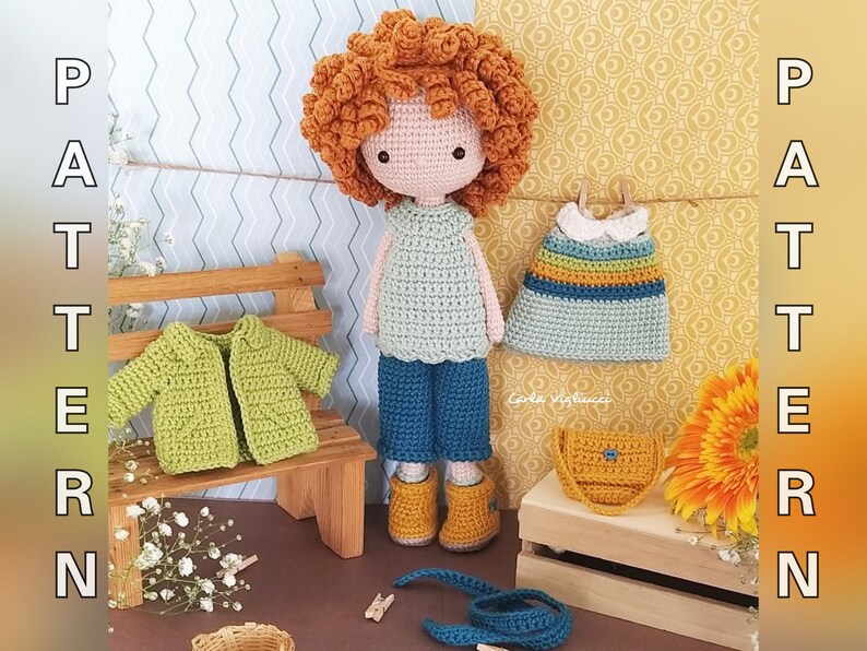 May include: Crochet doll with curly red hair wearing a green sweater, blue pants, and yellow boots. The doll is holding a blue and yellow striped dress and a yellow purse. The doll is sitting on a wooden bench with a green crocheted jacket on top.