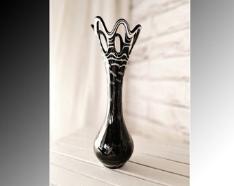 May include: A black and white striped glass vase with a unique, wavy design at the top. The vase is sitting on a white surface.