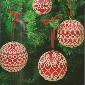 May include: Four red Christmas ornaments with white lace designs hanging on a green Christmas tree.