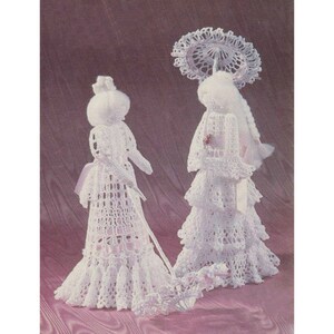 May include: Two crocheted dolls dressed in white gowns with lace trim. One doll is holding a crocheted parasol and the other is holding a crocheted walking stick.