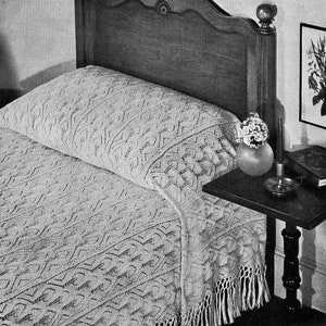 May include: A white crocheted bedspread with fringe on a wooden bed frame. The bedspread has a geometric pattern.