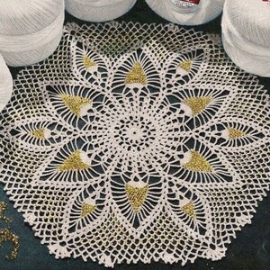 Puede incluir: Un mantel de encaje blanco con un delicado diseño floral y detalles dorados.
