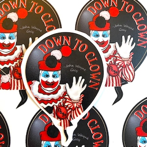 May include: A collection of stickers featuring a clown design. The stickers have a black background with the words "DOWN TO CLOWN" in red and white. The clown has red hair, a red nose, and a white face. The text "John Wayne Gacy" is also present.