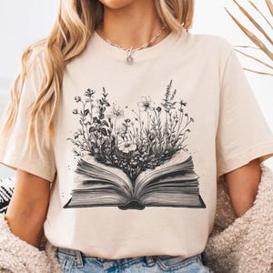 May include: A beige t-shirt with a black and white graphic of a book with flowers growing out of it.
