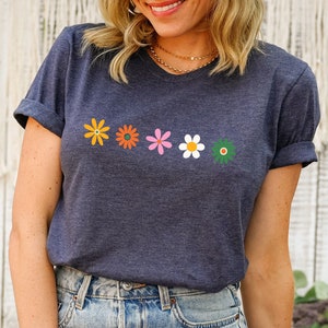 May include: A navy blue t-shirt with a row of five colorful flowers printed on the front. The shirt is made of a soft, comfortable material and has a relaxed fit.