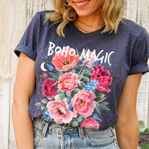 Może przedstawiać: Koszulka w ciemnoniebieskim kolorze z kwiatowym wzorem i napisem "boho magic" w białych literach.