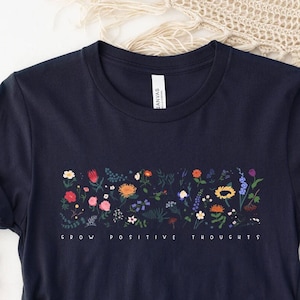 May include: Navy blue t-shirt with a floral design and the text "Grow Positive Thoughts".