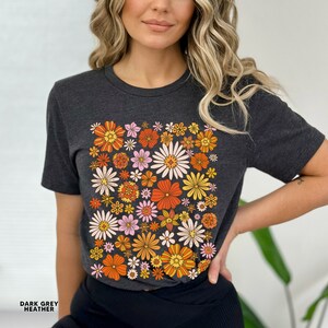 May include: A dark grey heather t-shirt with a colorful floral print. The print features a variety of flowers in shades of orange, yellow, pink, and white.