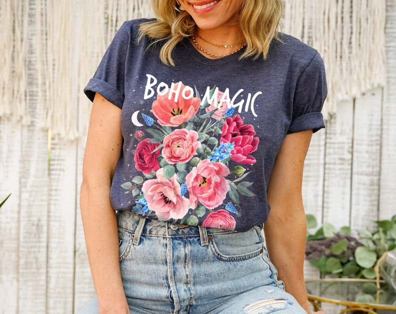 Może przedstawiać: Koszulka w ciemnoniebieskim kolorze z kwiatowym wzorem i napisem "boho magic" w białych literach.
