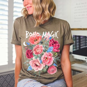 Może przedstawiać: Zielona koszulka z kwiatowym wzorem i napisem "boho magic" białymi literami.