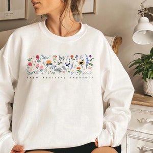 May include: White sweatshirt with a floral design and the text "Grow Positive Thoughts".
