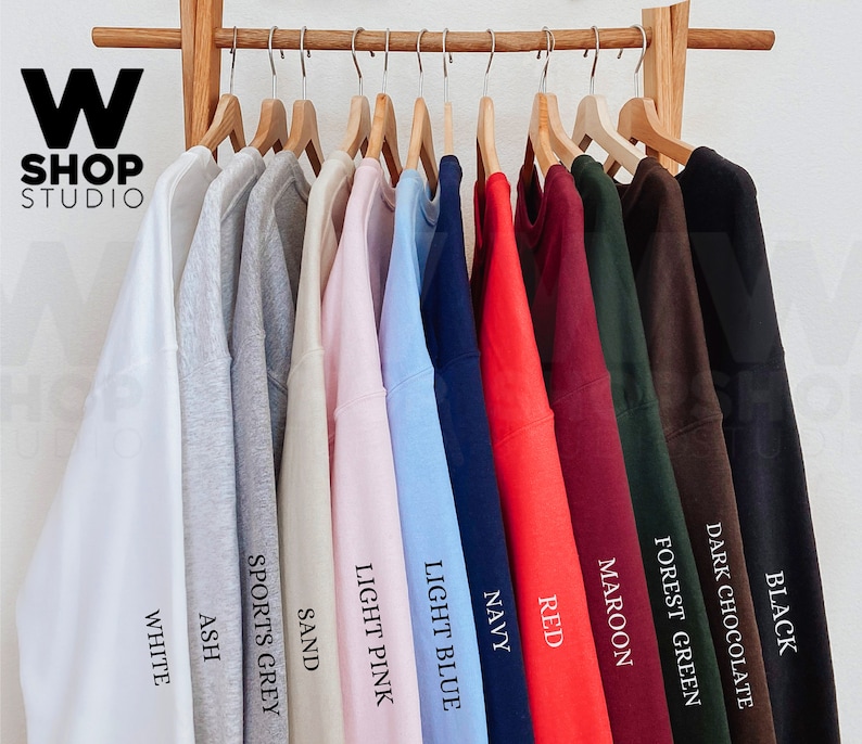 Op de afbeelding: Een rek met tien sweatshirts in verschillende kleuren, waaronder wit, as, sport grijs, zand, licht roze, lichtblauw, marine, rood, bordeaux, bosgroen, donker chocolade en zwart. De sweatshirts hangen aan houten hangers.