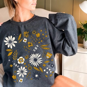 May include: A dark gray sweatshirt with a floral print featuring yellow, white, and black flowers on a gray background.