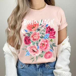 Może przedstawiać: R&oacute;żowy T-shirt z kwiatowym wzorem i napisem "BOHO MAGIC" białymi literami.