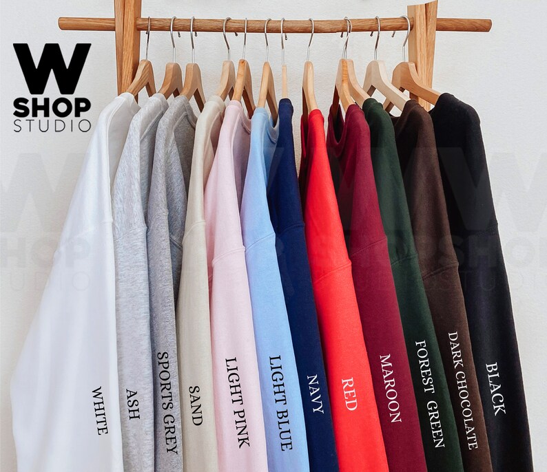 May include: Ten different colored sweatshirts hanging on wooden hangers. The colors are white, ash, sports grey, sand, light pink, light blue, navy, red, maroon, forest green, dark chocolate, and black.