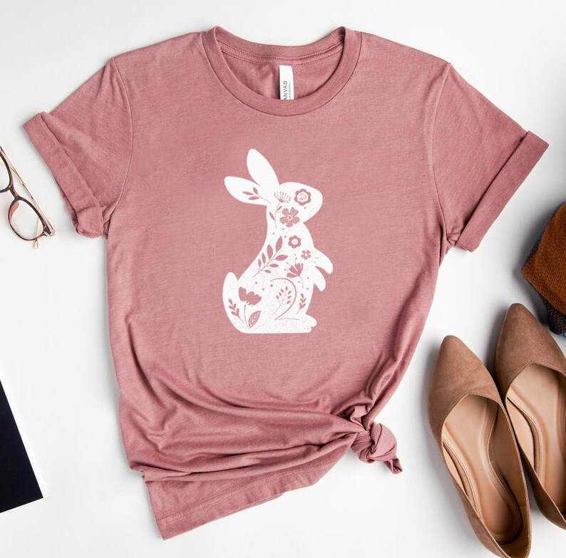 K&ouml;nnte beinhalten: Ein mauvefarbenes T-Shirt mit einem wei&szlig;en floralen Hasendesign. Der Hase ist wei&szlig; umrandet und mit wei&szlig;en floralen Details gef&uuml;llt.