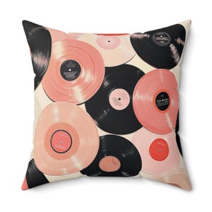 May include: A square throw pillow with a white background and a pattern of pink and black vinyl records. The records are arranged in a random pattern and overlap each other.