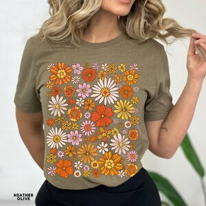 May include: A green t-shirt with a retro floral print featuring orange, yellow, pink, and white flowers.