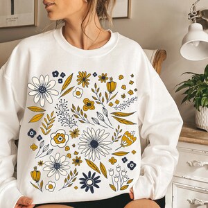 May include: White sweatshirt with a floral pattern in yellow, white, and blue. The flowers are stylized and have a vintage feel.