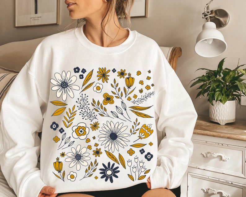 May include: White sweatshirt with a floral pattern in yellow, white, and blue. The flowers are stylized and have a vintage feel.