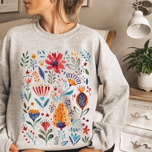 May include: A gray sweatshirt with a colorful floral print. The print features a variety of flowers, leaves, and stems in shades of red, orange, yellow, blue, and green.