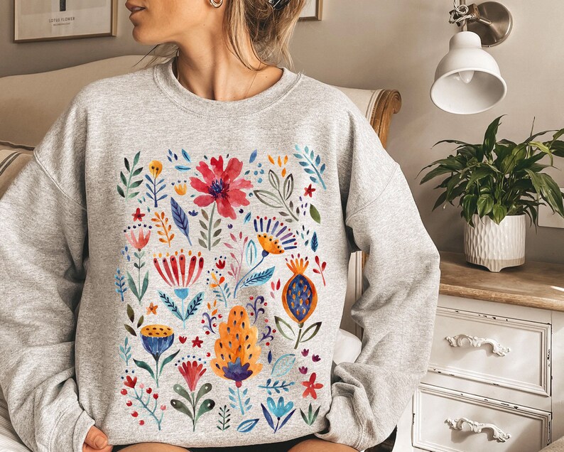 May include: A gray sweatshirt with a colorful floral print. The print features a variety of flowers, leaves, and stems in shades of red, orange, yellow, blue, and green.