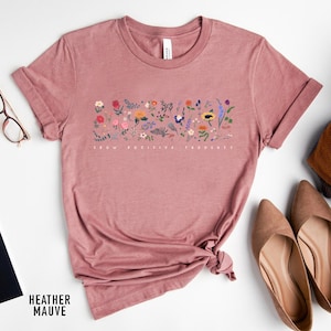 May include: A heather mauve t-shirt with a floral design and the text "Grow Positive Thoughts".