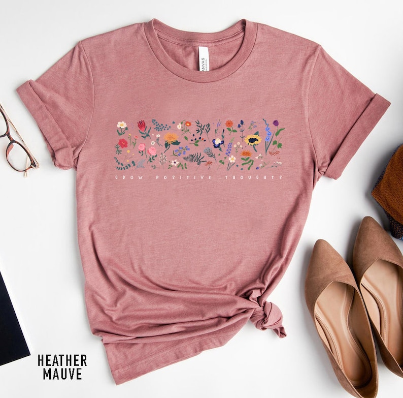 May include: A heather mauve t-shirt with a floral design and the text "Grow Positive Thoughts".