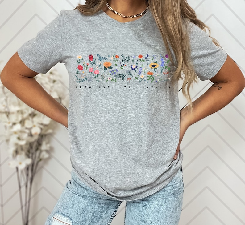 May include: A heather grey t-shirt with a floral design and the text "Grow Positive Thoughts".
