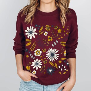 May include: A maroon sweatshirt with a floral print featuring white, yellow, and blue flowers on a burgundy background.