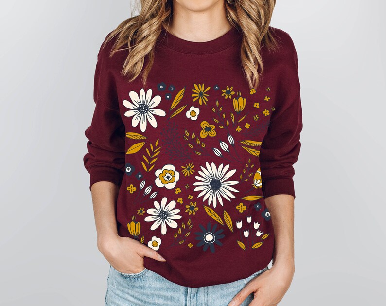 May include: A maroon sweatshirt with a floral print featuring white, yellow, and blue flowers on a burgundy background.