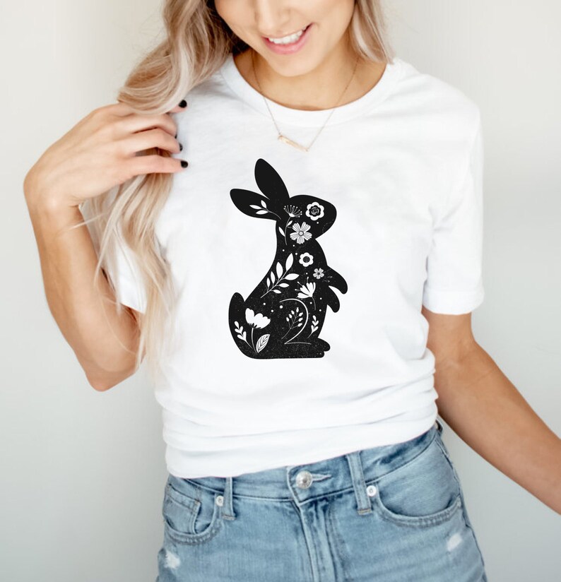 K&ouml;nnte beinhalten: Ein wei&szlig;es T-Shirt mit einer schwarzen Silhouette eines Kaninchens, das mit wei&szlig;en Blumenmustern gef&uuml;llt ist.
