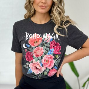 Może przedstawiać: Szary t-shirt z nadrukiem kwiatowym i napisem "boho magic" w kolorze białym. Kwiaty są r&oacute;żowe, czerwone i niebieskie.